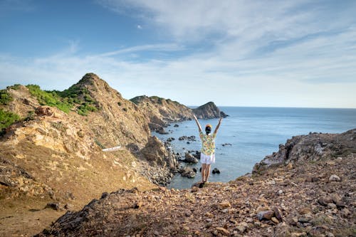 Unrecognizable person raising arms on rocky bay shore