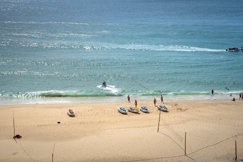 Relaxed people in life jackets walking on warm sandy beach near wave runners on sunny summer day