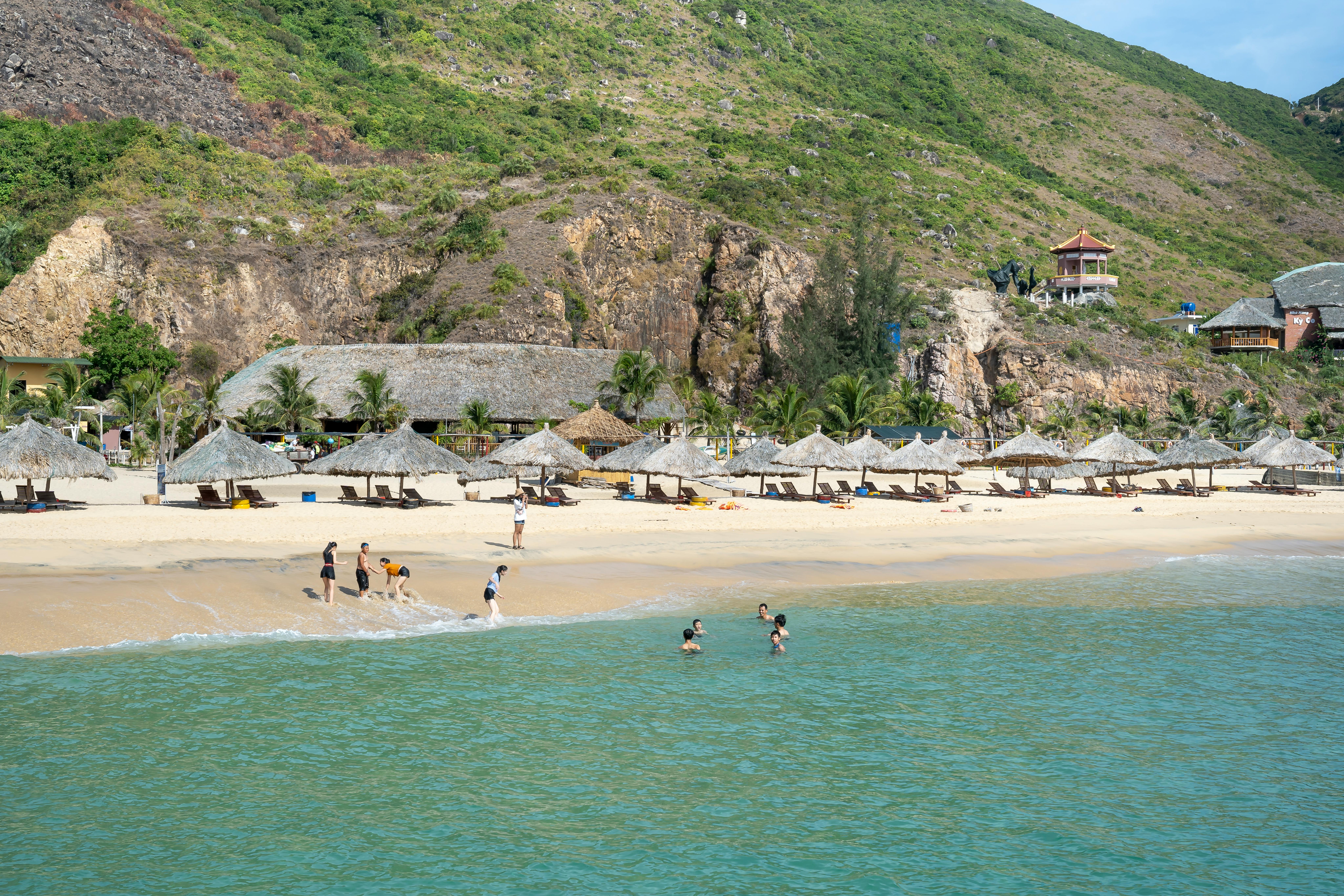 people chilling on sandy beach surrounded by grassy hills