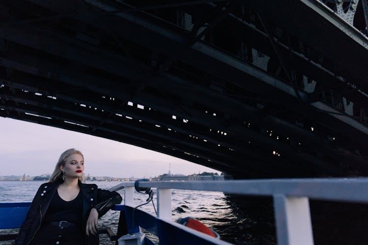 A Woman In Black Leather Jacket Sitting On A Boat Sailing On A River