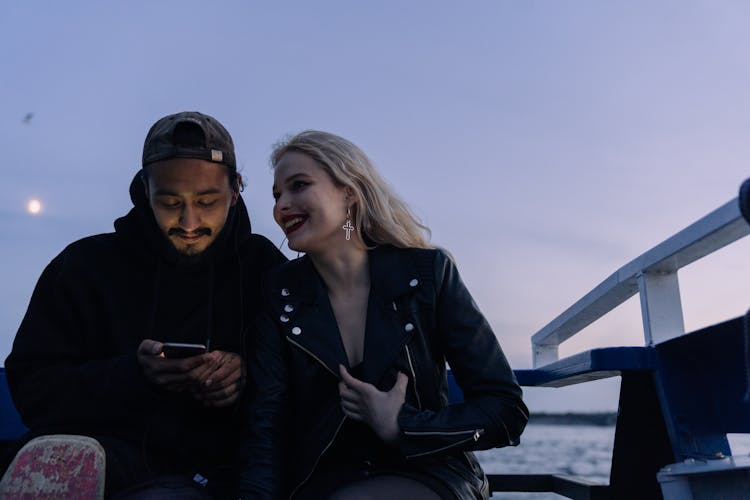 A Couple Sitting On The Deck Of A Boat Under Evening Sky