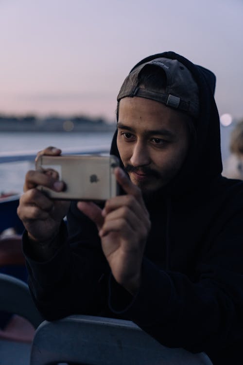 A Man in Black Hoodie Taking Photos Using Cellhpone