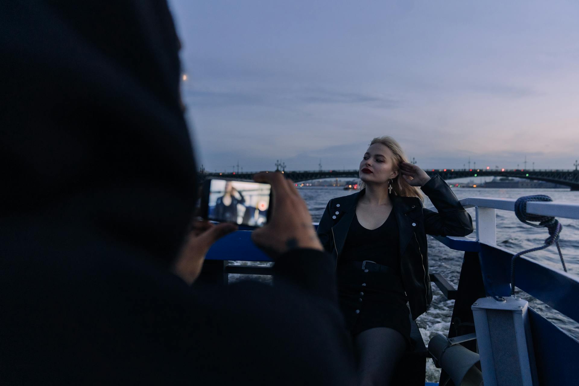 Stylish woman posing on a boat at twilight, captured on camera by a photographer.