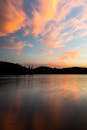 Silhouettes of forest and hills near clean peaceful lake under bright cloudy sky in late dusky evening