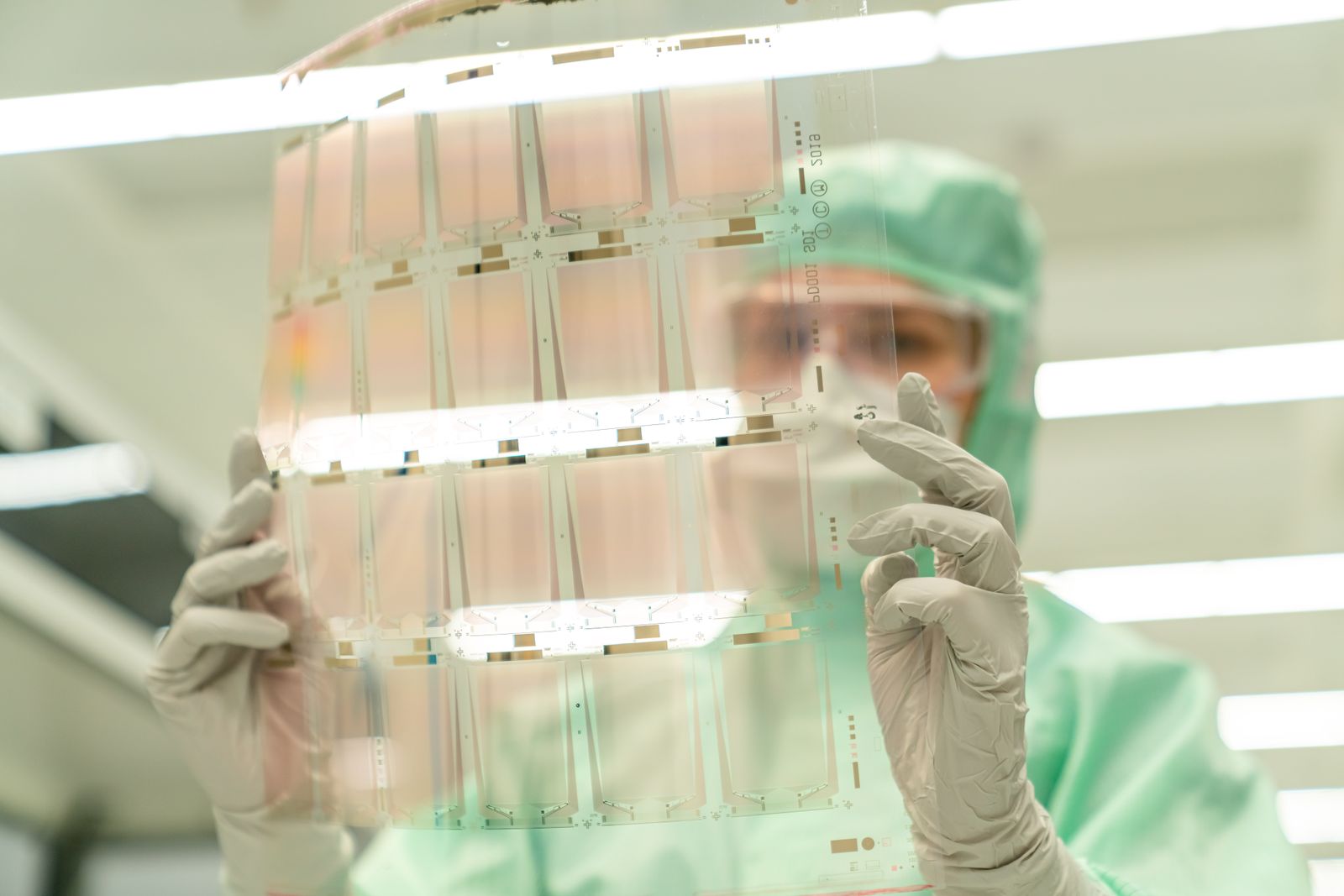 Technician in protective gear inspecting a transparent sheet in a laboratory