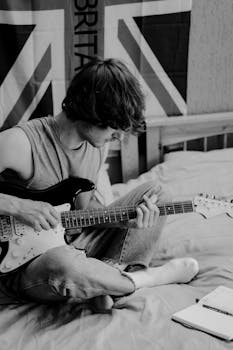 一张黑白照片里，一名年轻人在室内弹着电吉他，背景是英国国旗
