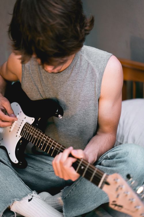 Free Casual young man in stylish attire playing an electric guitar indoors, showcasing creativity and relaxation. Stock Photo