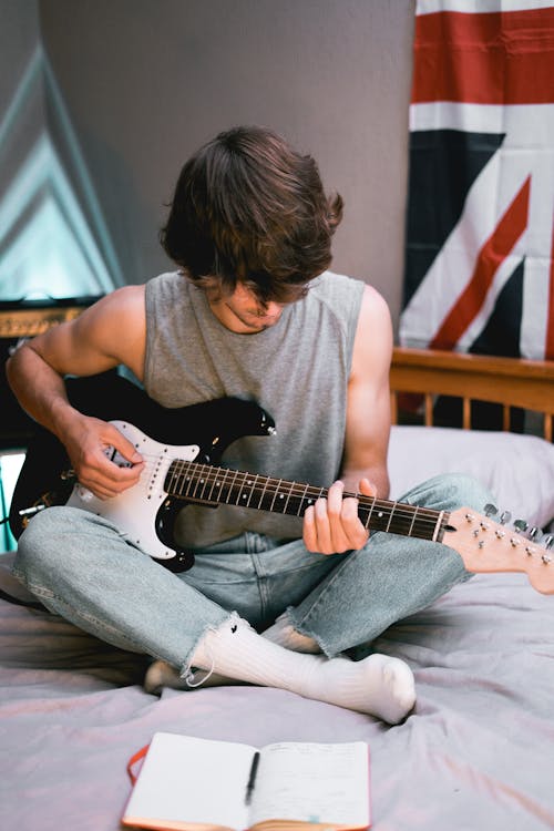 Man in Gray Tank Top Playing Black and White Stratocaster Electric Guitar