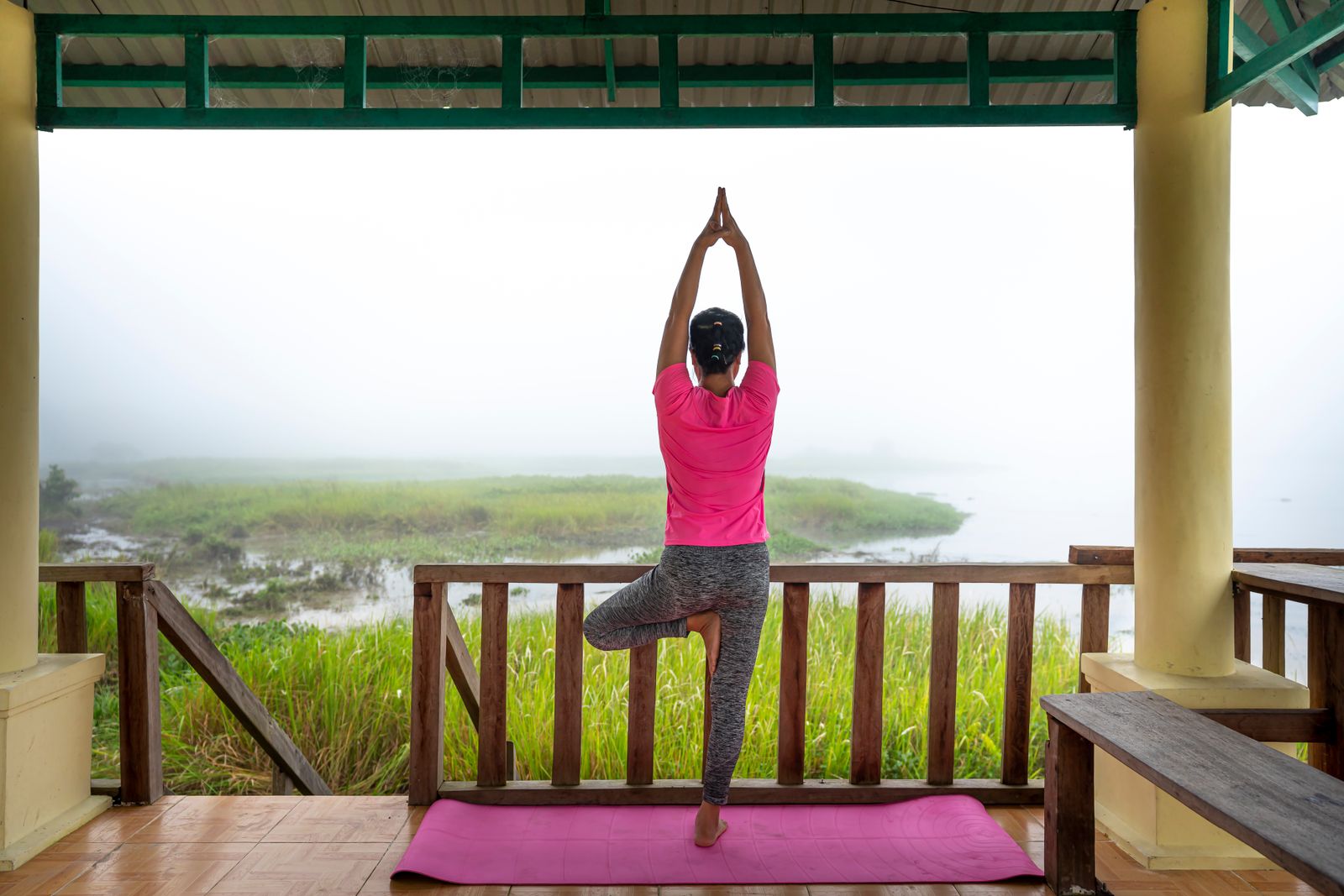 Woman practicing Vrksasana tree pose on a terrace, balancing on one leg with hands overhead