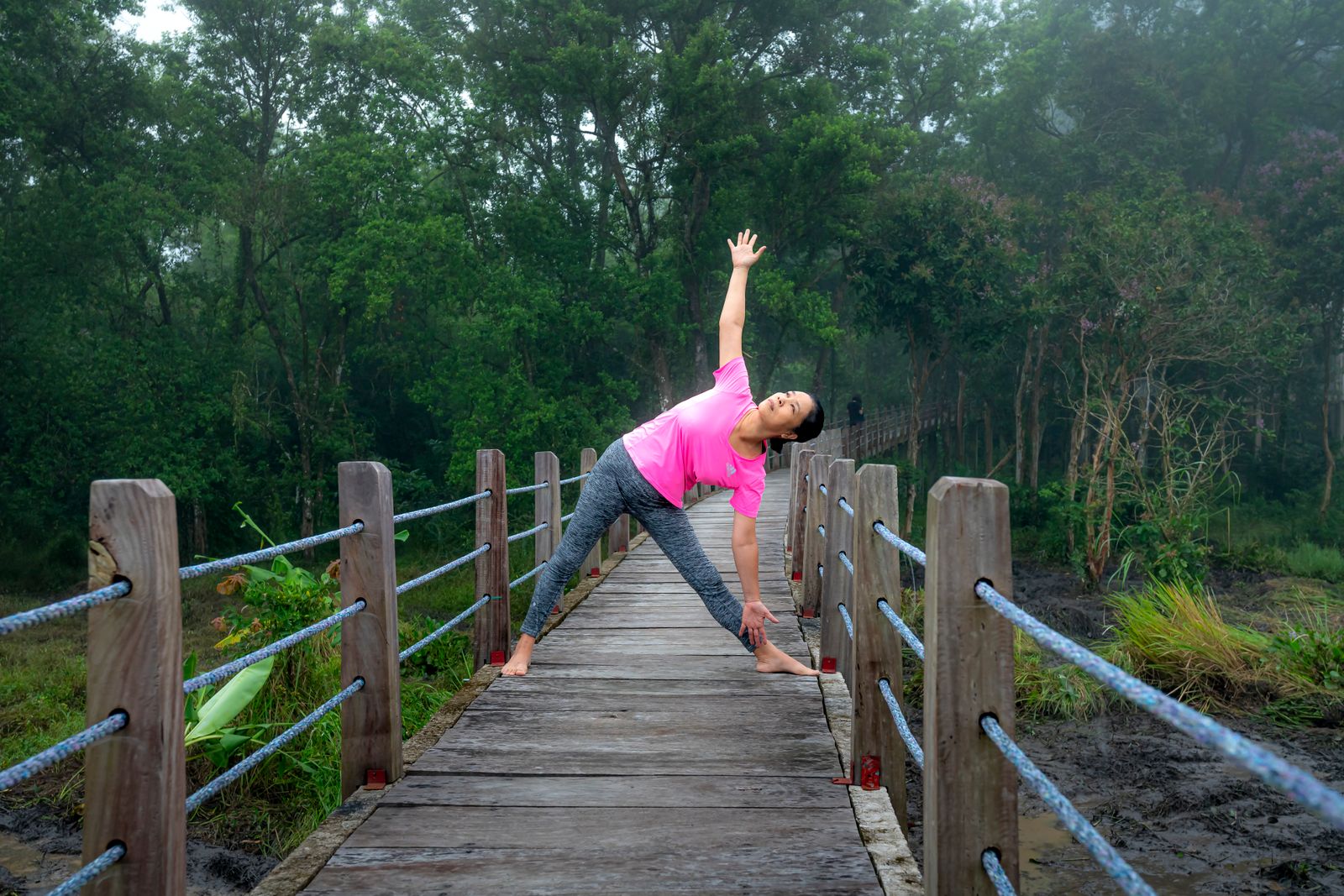 Woman in activewear practicing trikonasana triangle pose outdoors with arms extended