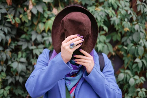 Faceless woman hiding face behind hat in park