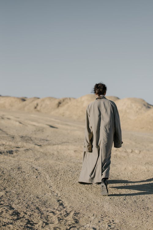 Man in Gray Coat Walking on Brown Sand