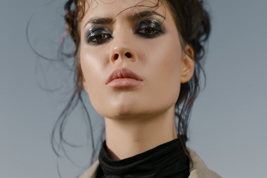 Close-up portrait of a woman with intense eye makeup and strong facial expression outdoors.