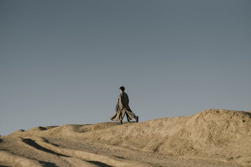 Man in Black Jacket Walking on Brown Sand