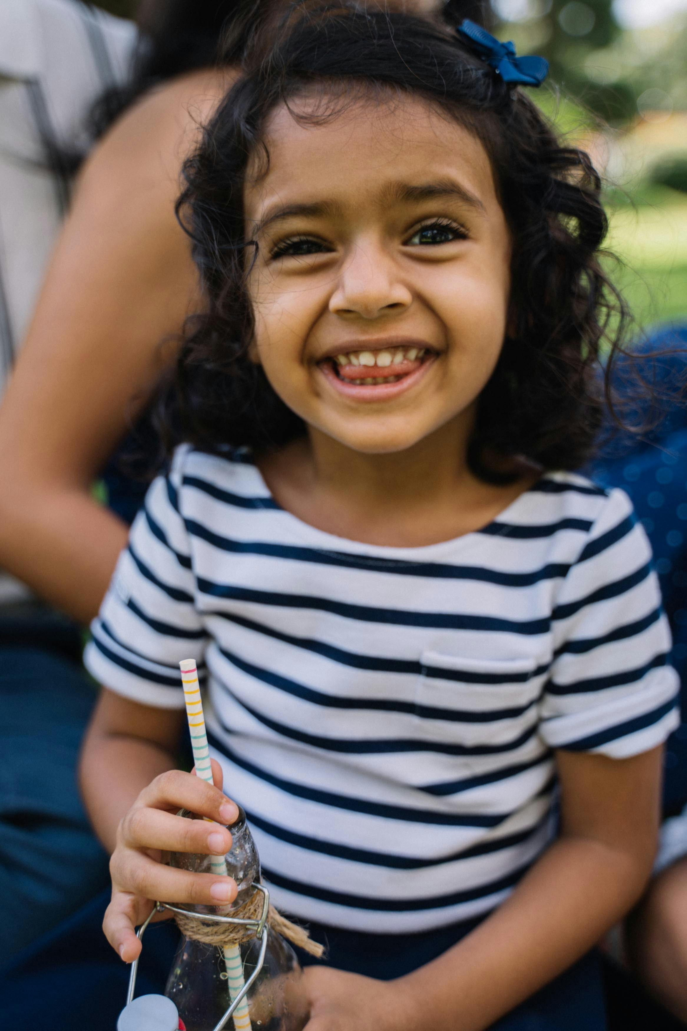 一个穿着条纹衬衫的快乐年轻女孩，在阳光明媚的户外拿着瓶子微笑