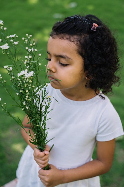 A Girl in White Dress Smelling a Bunch of Flowers