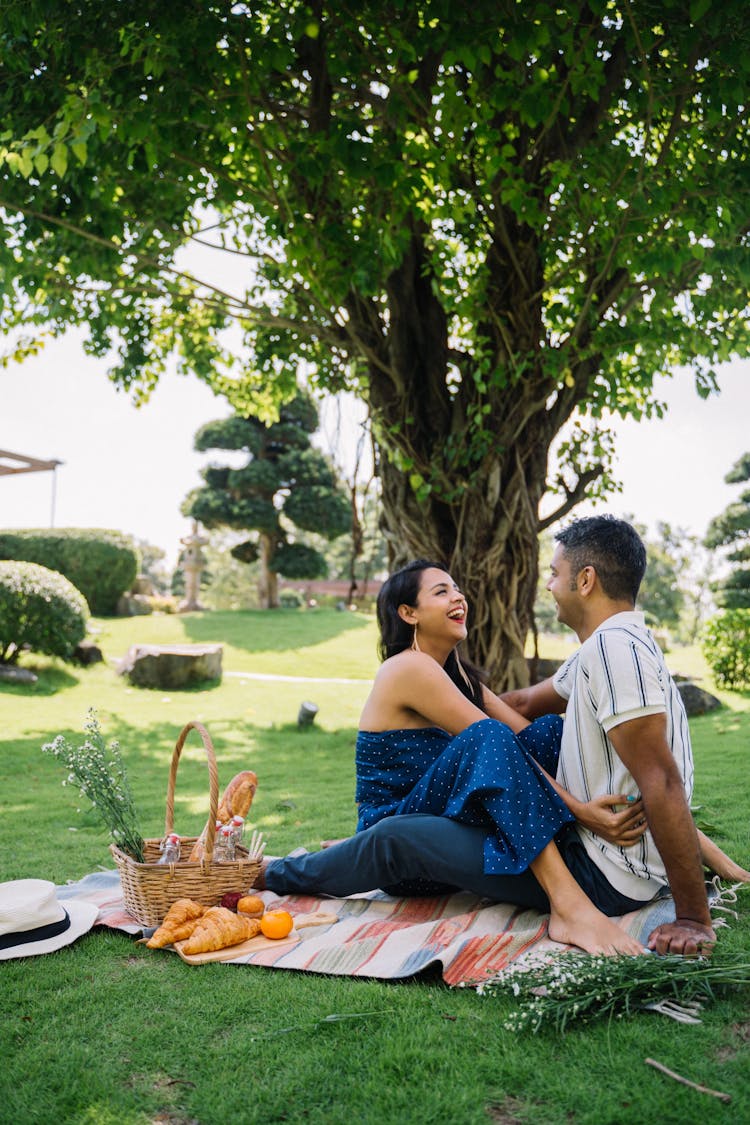 A Couple Sitting On Picnic Mat Near A Tree