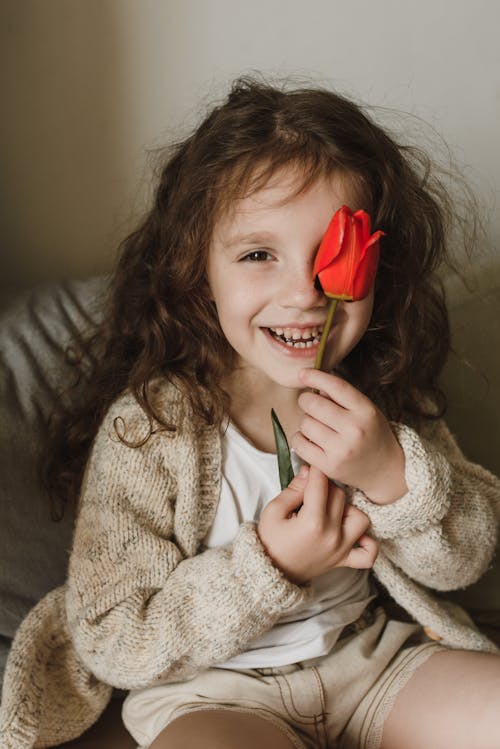 Free Girl in Beige Sweater Holding a Red Flower Stock Photo