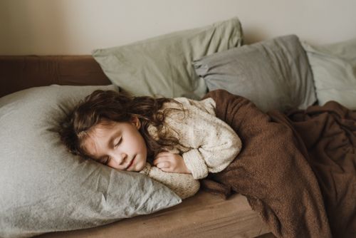 Free A young girl sleeping peacefully covered with a warm blanket indoors. Stock Photo
