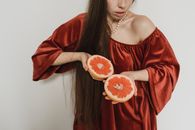 一名身穿红色连衣裙的女子手拿一片葡萄柚，展示着新鲜的柑橘类水果