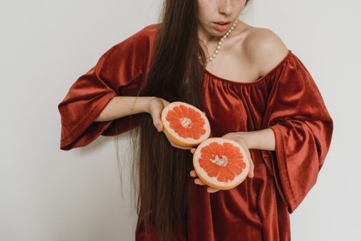 一名身穿红色连衣裙的女子手拿一片葡萄柚，展示着新鲜的柑橘类水果