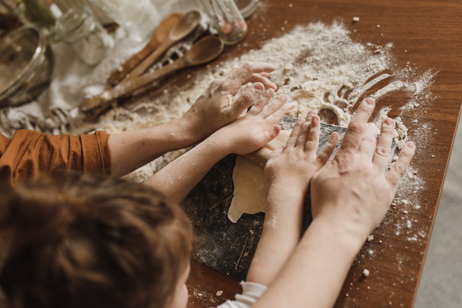 A parent and child bonding while kneading dough in a messy kitchen environment.
