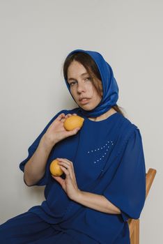 一位身着蓝色连衣裙、头戴头巾、手持柠檬的女性肖像，背景朴素