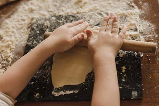 Close-up of child rolling dough with a wooden pin, showcasing hands-on cooking.