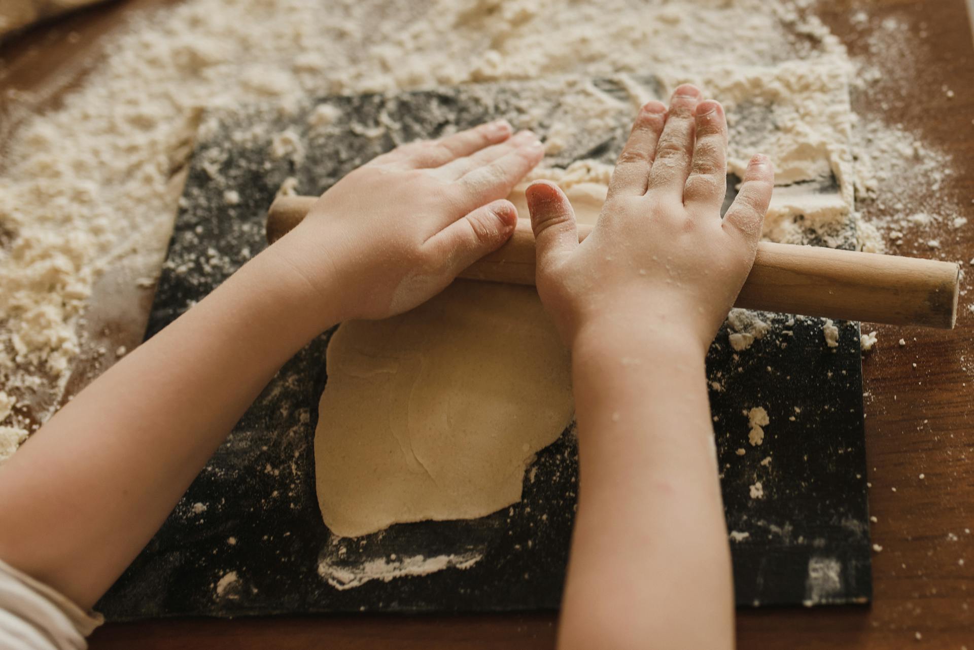 Close-up of child rolling dough with a wooden pin, showcasing hands-on cooking.