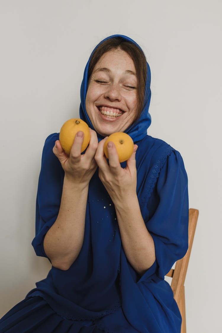 A Woman In Blue Hijab Holding Oranges