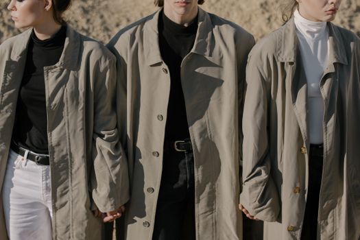 Three stylish adults in trench coats exude urban fashion chic as they hold hands outdoors.