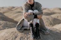 一位时尚女性穿着风衣、白裤子和靴子，坐在沙滩上
