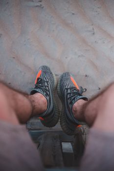 Top view of crop unrecognizable male in trendy footwear sitting above sandy coast
