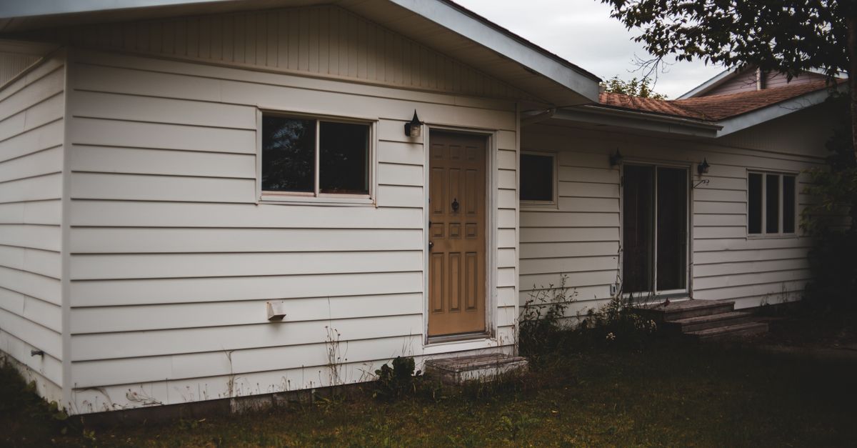 Small poor building exterior with ribbed walls near grass meadow and tree under cloudy sky