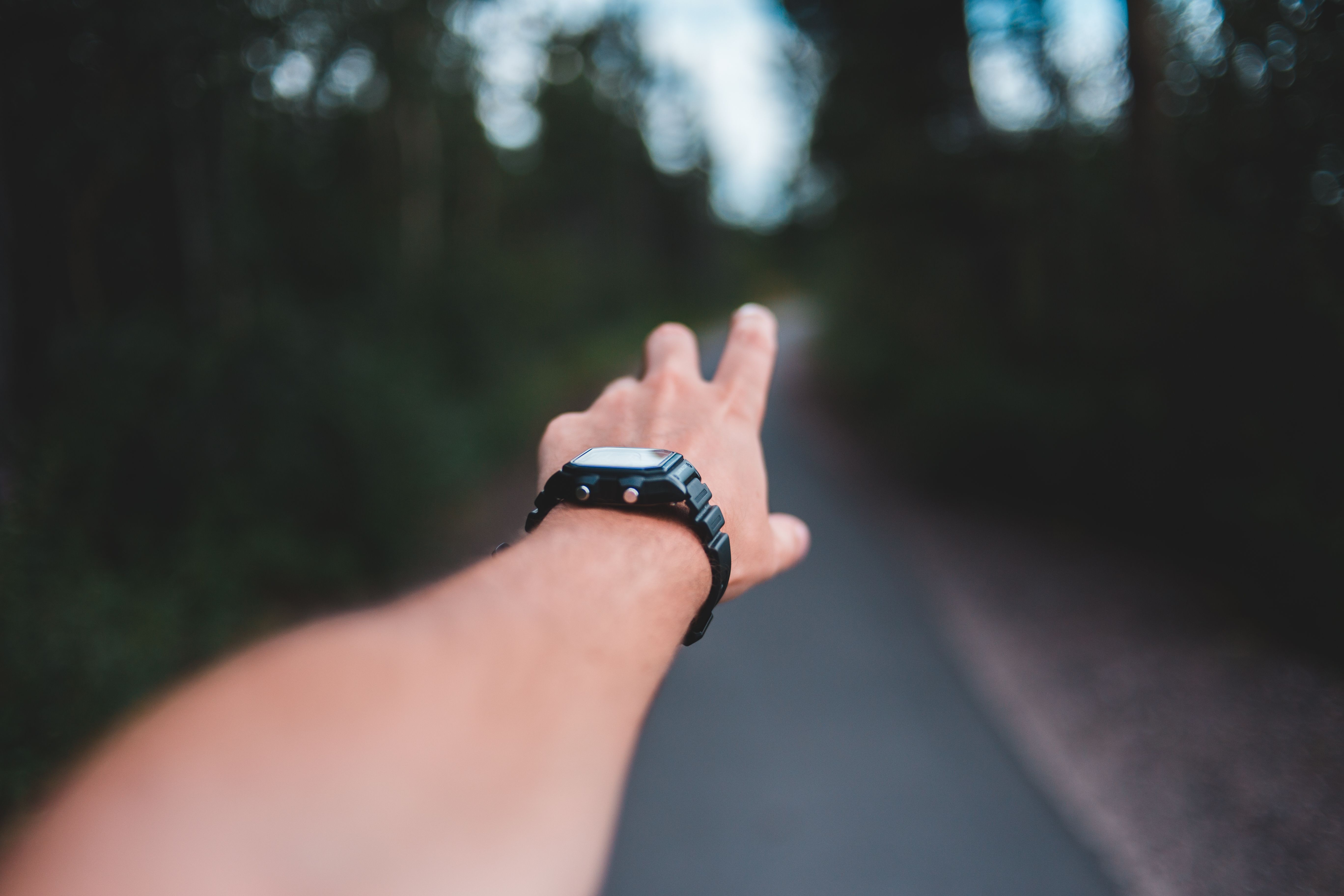 Crop anonymous male in stylish black wristwatch reaching arm on asphalt roadway between trees