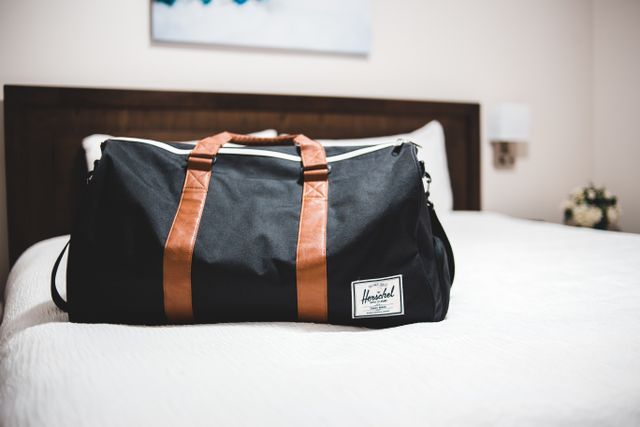 Black duffel travel bag with leather trim on a soft neutral surface