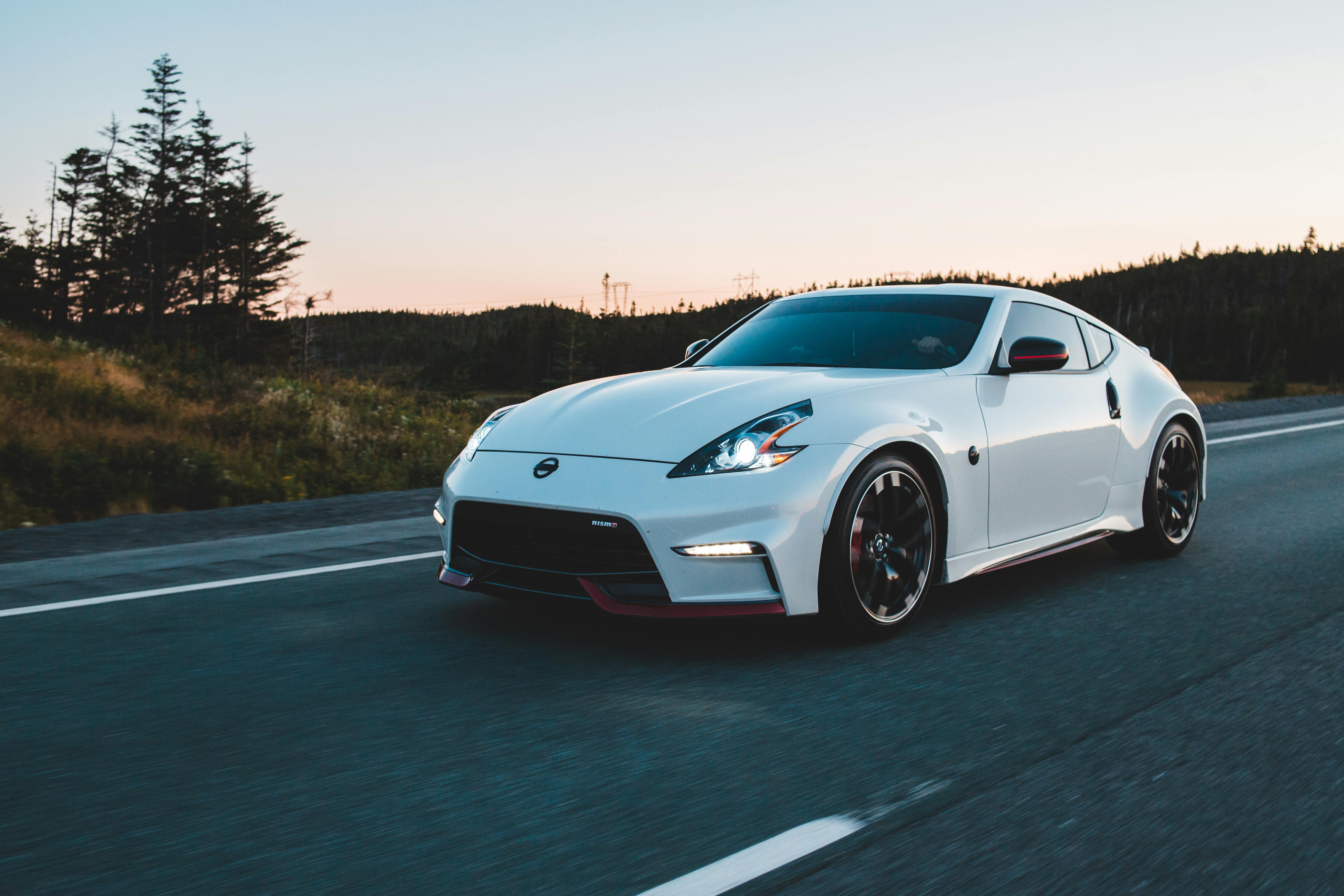 A luxury white sports car speeds along a scenic forested highway at dusk.