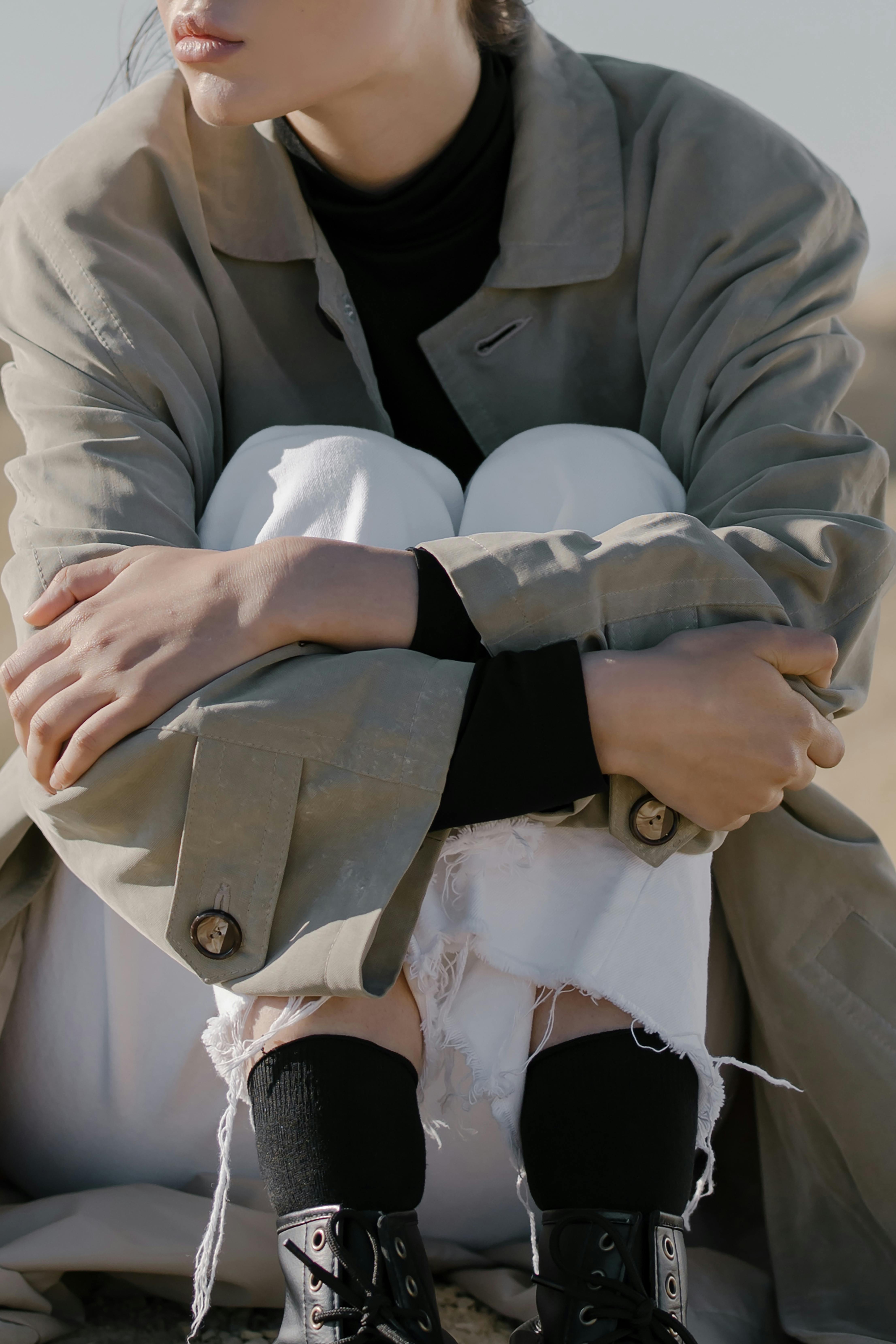 person in beige coat and white pants sitting