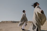 在广阔的沙漠环境中，两名穿着风衣的模特巧妙地摆出姿势