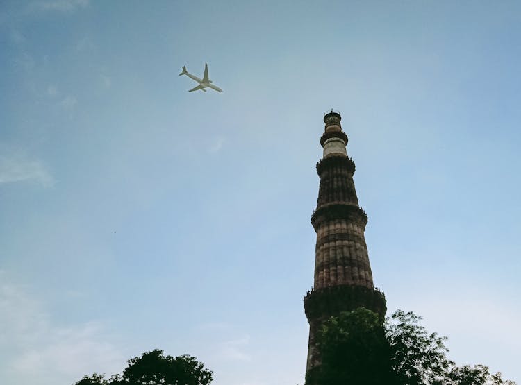 An Airplane In The Blue Sky Over A Concrete Tower