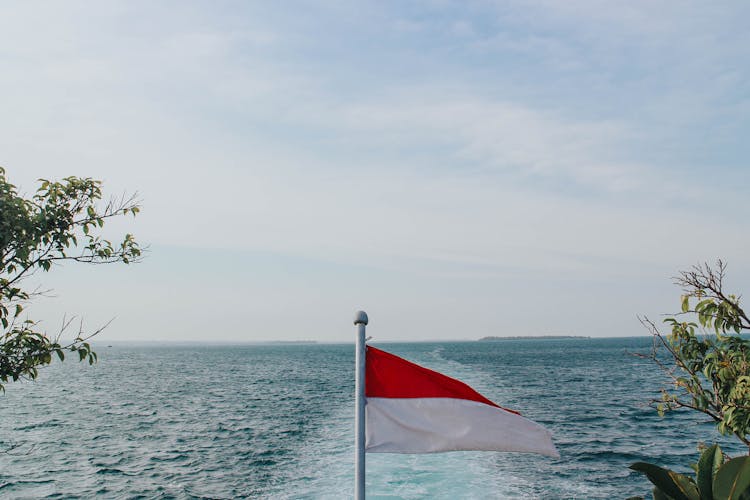 Red And White Flag On Pole Near Body Of Water