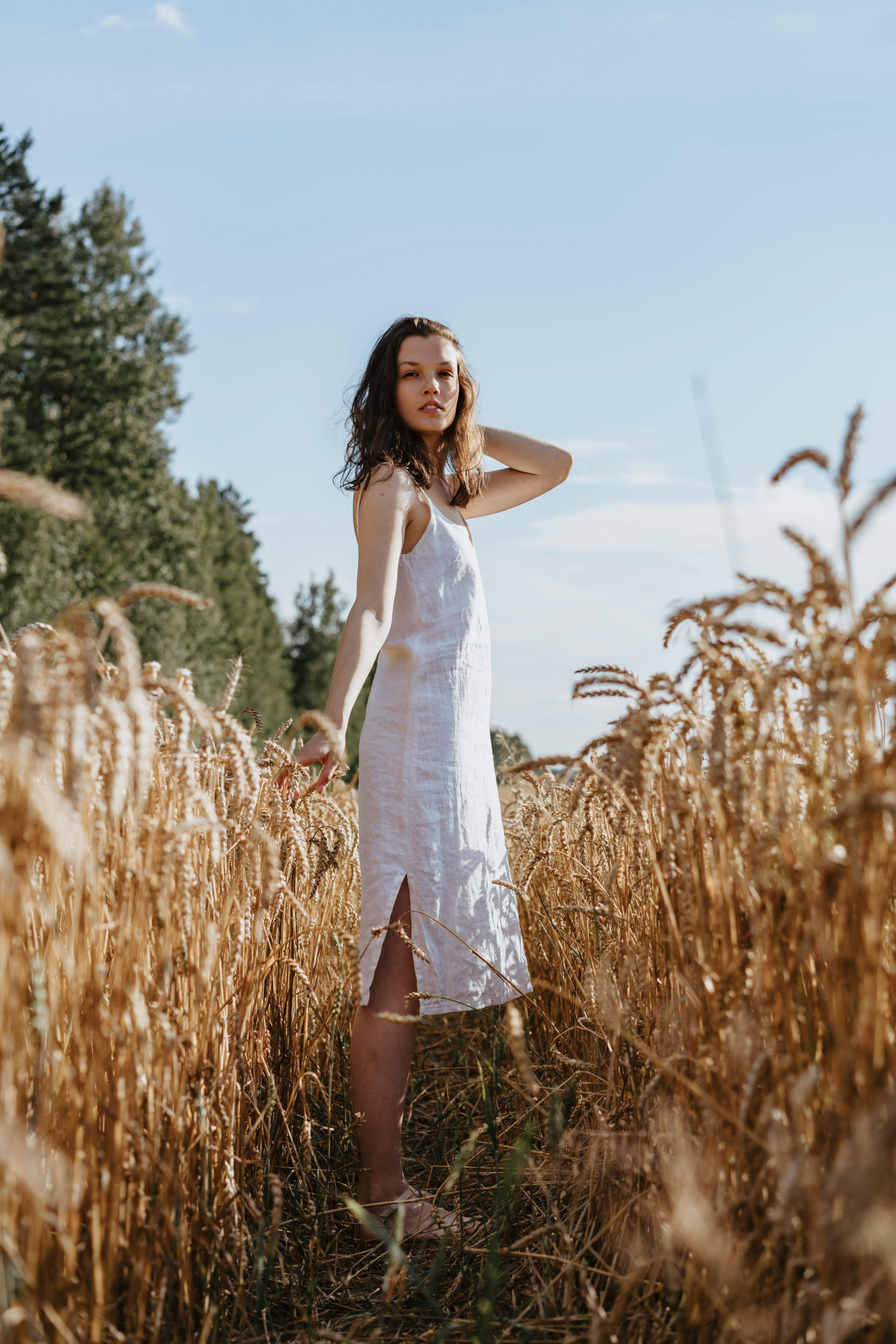 蔚蓝的天空下，一位身穿白裙的女子站在金色的小麦中间的宁静场景