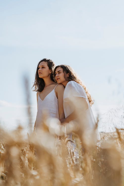 Two Women in White Dress Standing on Brown Grass Field