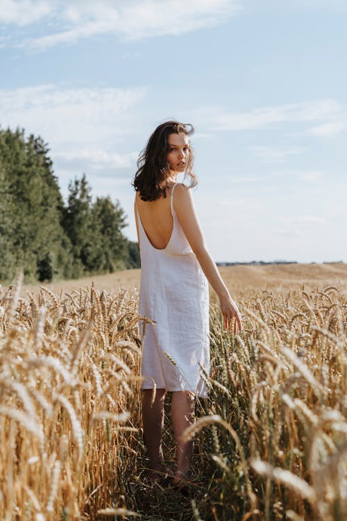 Woman in White Spaghetti Strap Dress Standing on Brown Grass Field
