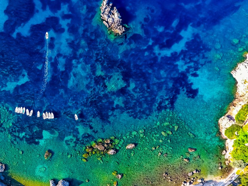 Incredible Private Helicopter Transfer from Folegandros to Santorini Review 2026 - Stunning aerial view of turquoise waters and boats along Paleokastritsa coast in Greece.