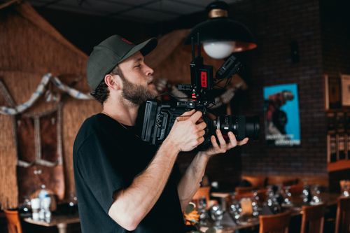 Free Cinematographer holding a camera rig on a film set, capturing a scene indoors. Stock Photo