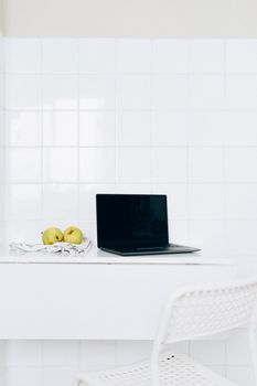 A sleek workspace featuring a laptop and apples on a white desk against a tiled wall.