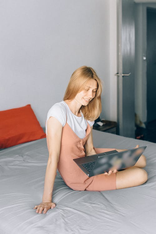 Free A Woman Sitting on Her Bed while Holding Her Laptop Stock Photo