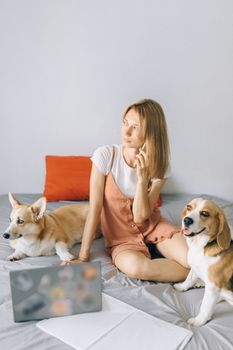 Young woman using phone with two dogs by her side on bed, working from home setup.