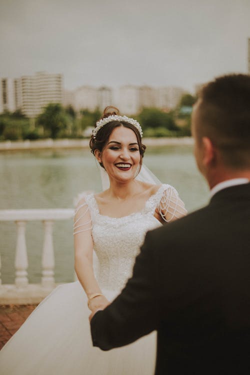 Cheerful bride and fiance holding hands on lakeside